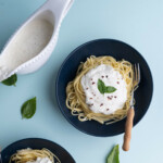 Two bowls of cooked linguine with ricotta sauce served on top and garnished with crushed red pepper and fresh basil.