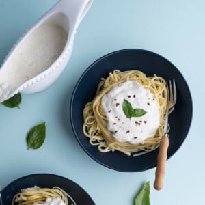 Two bowls of cooked linguine with ricotta sauce served on top and garnished with crushed red pepper and fresh basil.