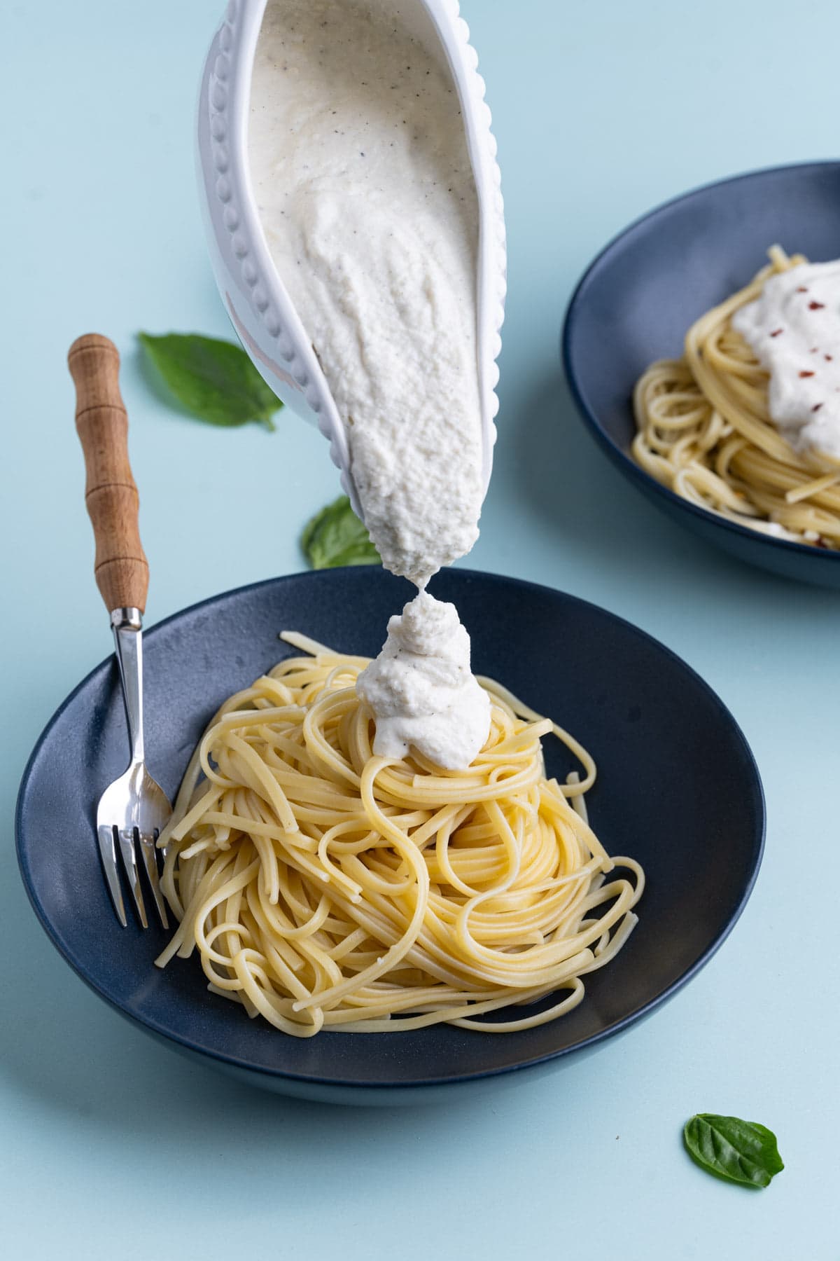 Adding Ricotta cheese sauce to a bowl of linguine pasta. 