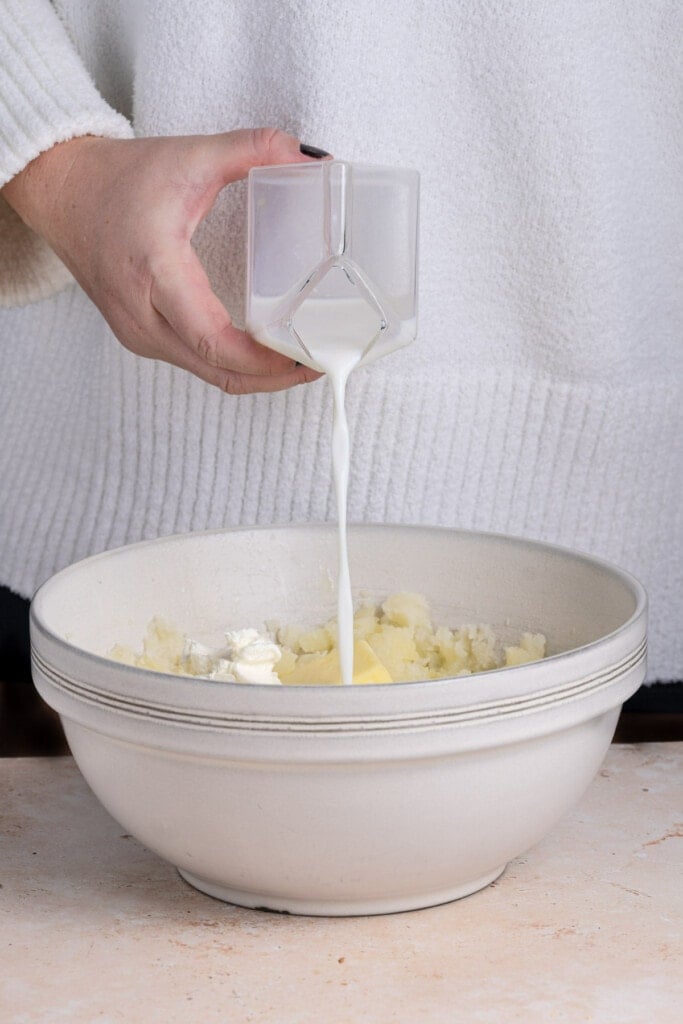 Adding milk to smashed potatoes to whip.