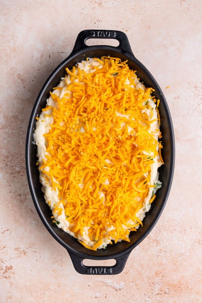 Mashed potatoes in a casserole dish topped with a layer of shredded cheddar cheese. 
