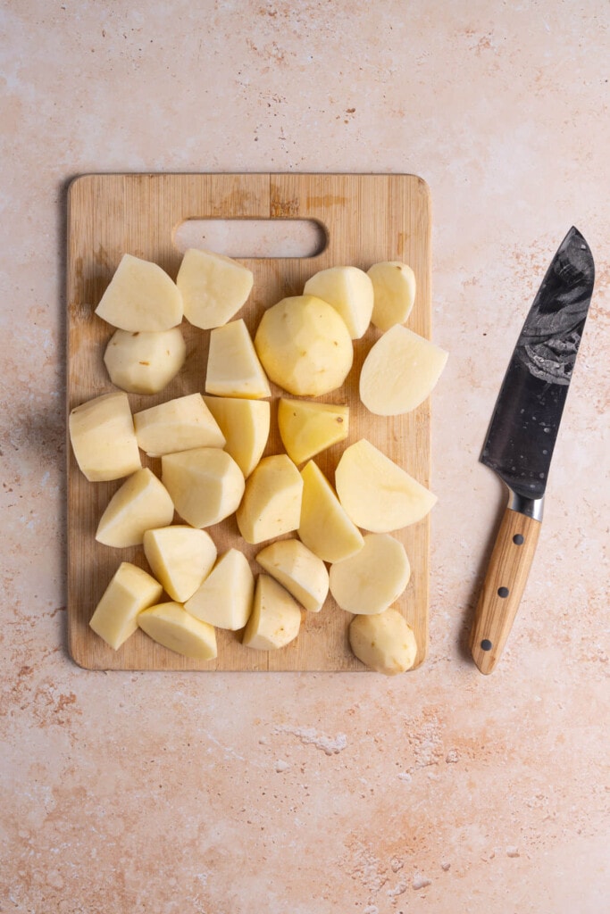 Peeled and chopped russet potatoes on a chopping board next to a sharp knife. 