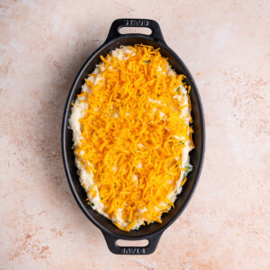 Mashed potatoes in a casserole dish topped with a thin layer of shredded cheddar cheese.