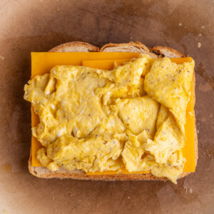 Scrambled egg layered on top of cheese and bread frying in a pan.
