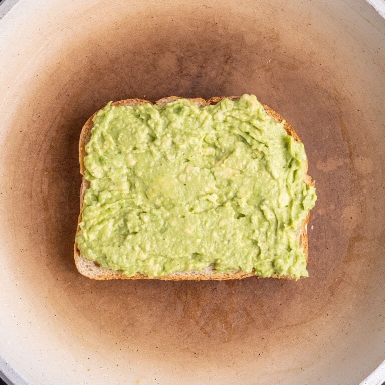 Slice of buttered bread in a pan buttered side down and smashed avocado side up.