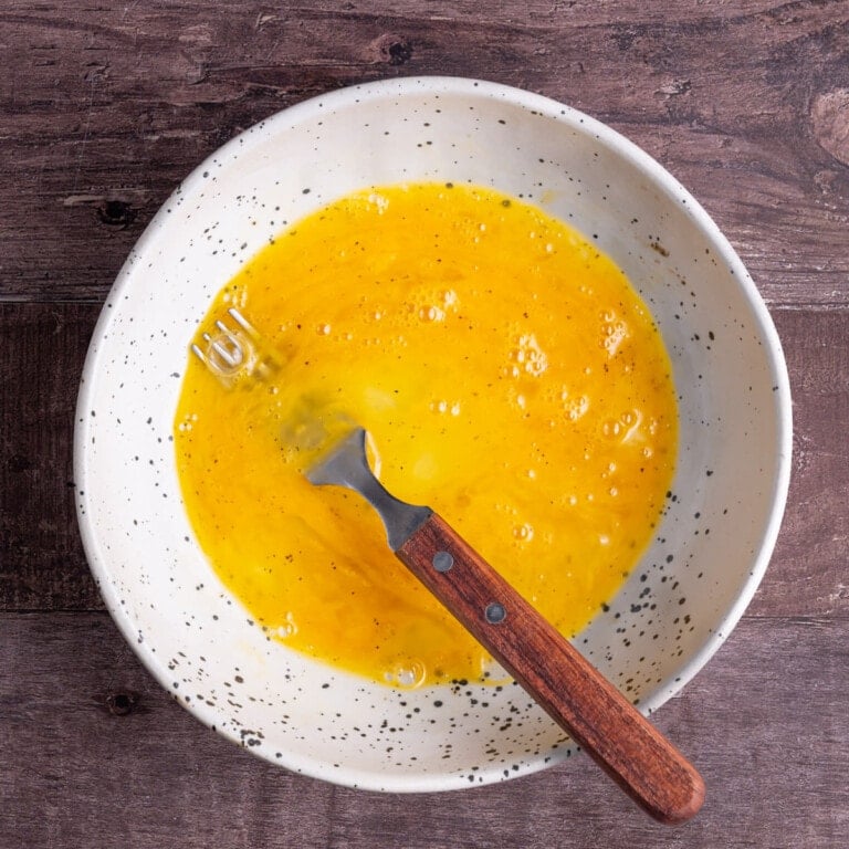 Egg whites and yolks beaten together with a fork in a bowl.