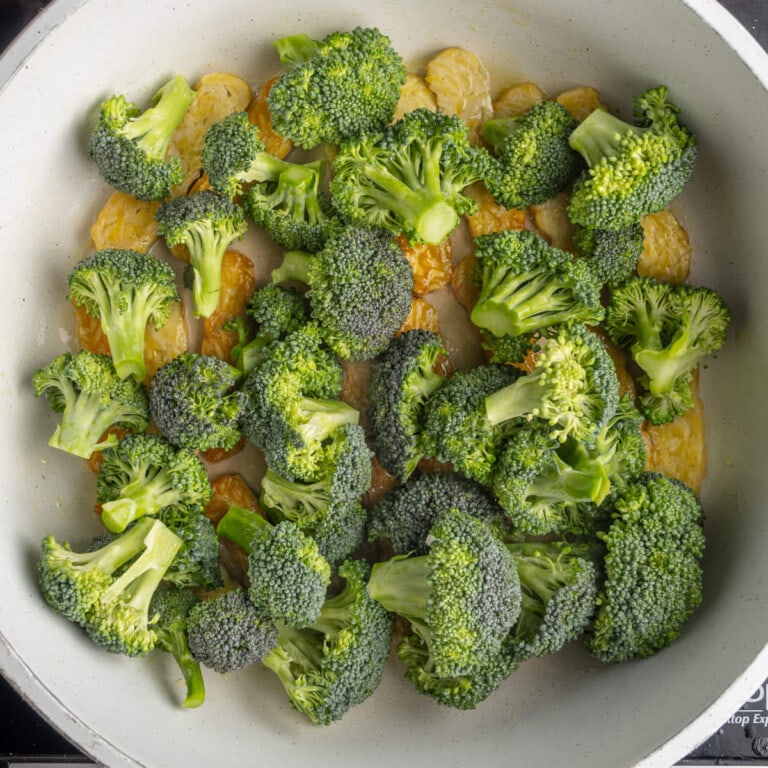 Broccoli steaming on top of frying tempeh.