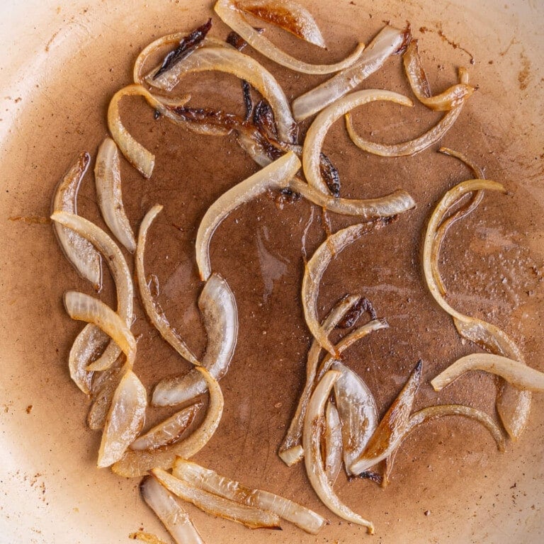 Sliced onions frying in a pan over medium heat.