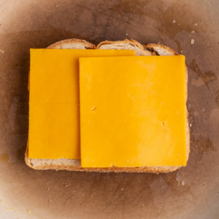 Buttered bread frying in a pan with two slices of cheese placed on top.