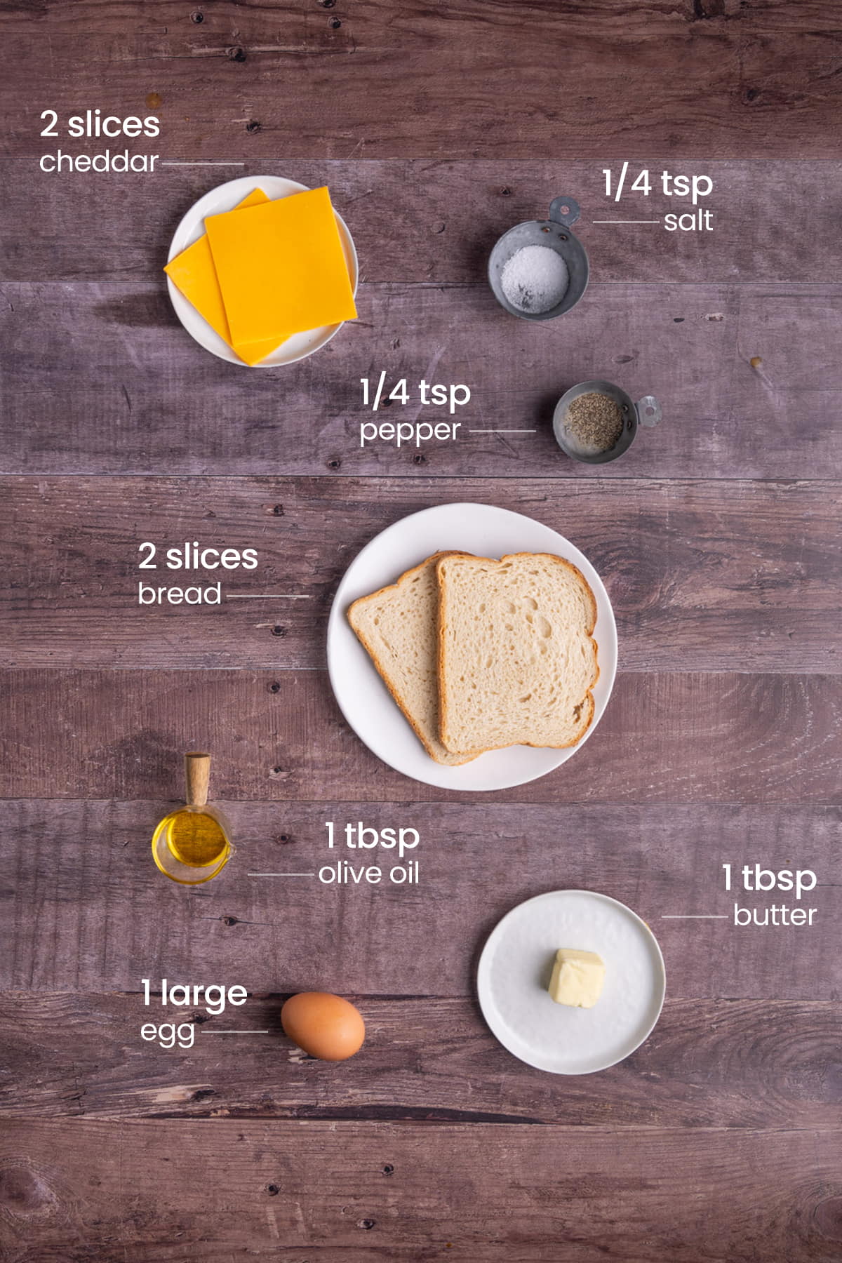 all ingredients for classic fried egg and cheese breakfast sandwich - cheddar cheese, salt, pepper, bread, olive oil, butter, egg