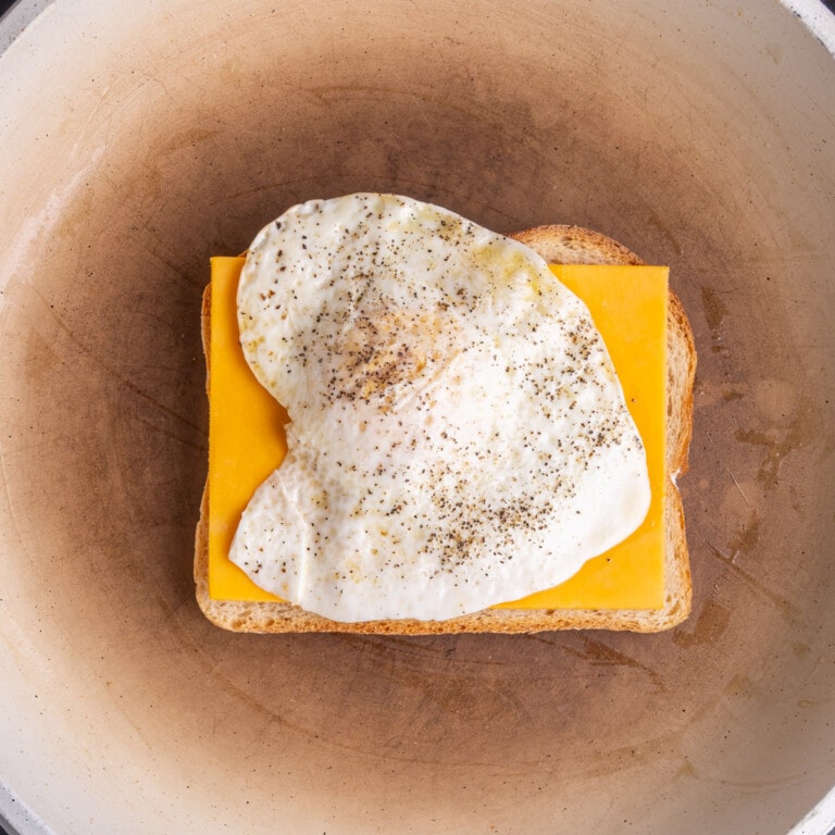 Fried egg stacked on top of cheddar cheese on toasting bread.