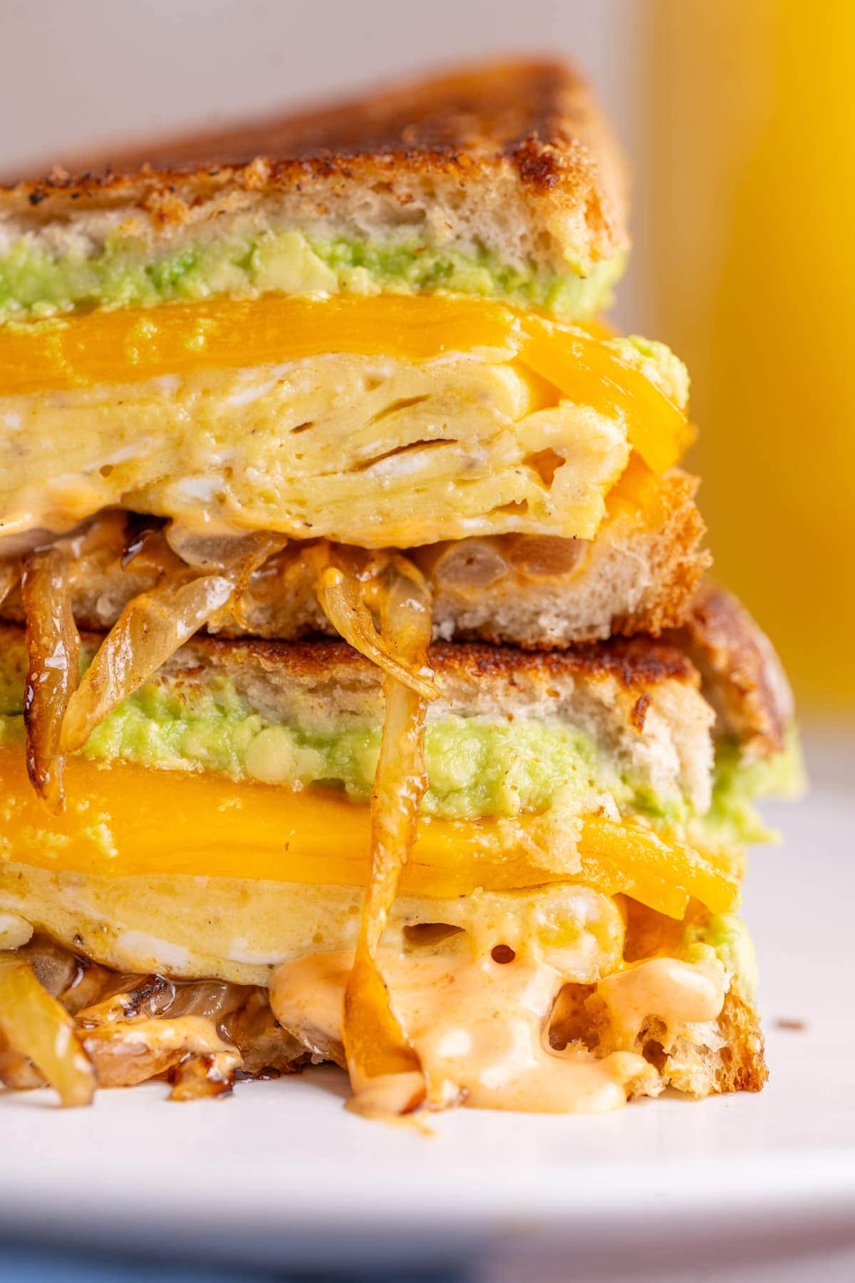Close up of loaded breakfast sandwich with avocado, cheese, egg, onions, and spicy mayo.