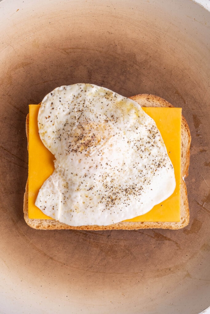 Fried egg stacked on top of cheese and bread frying in a pan. 