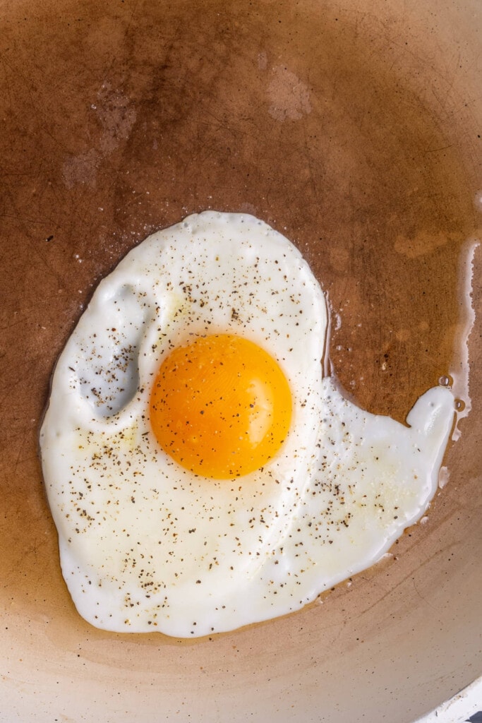 Egg cracked in a hot pan with oil topped with salt and pepper.