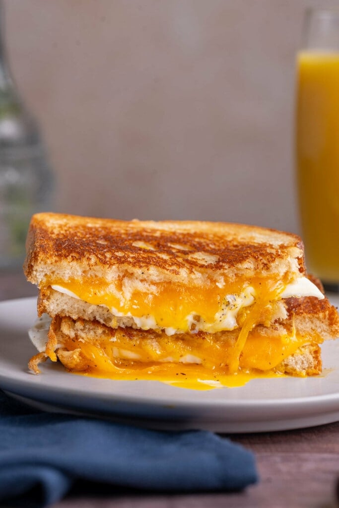 Fried egg and cheese sandwich sliced in half and served stacked on a white plate. 