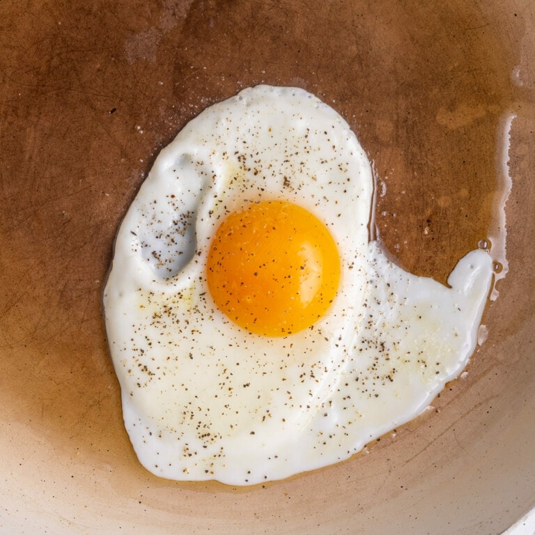 Egg with salt and pepper frying in oil on a frying pan.