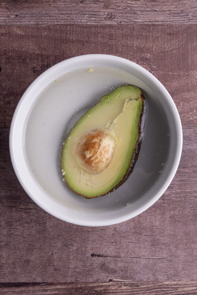 Covering half an avocado with water in a bowl to save it for later.