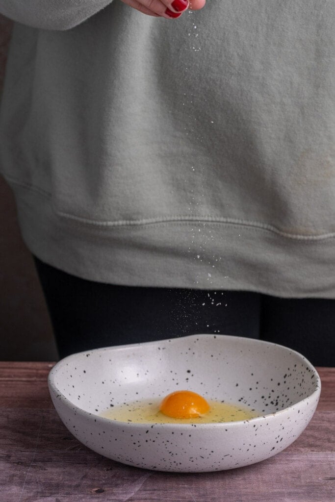 Adding salt to eggs in a bowl to season them before scrambling them. 