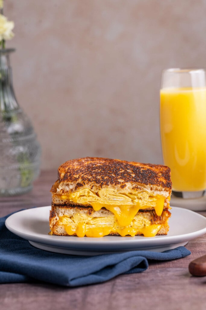 Scrambled egg and cheddar cheese breakfast sandwich sliced in half with two halves stacked atop one another on a plate. 