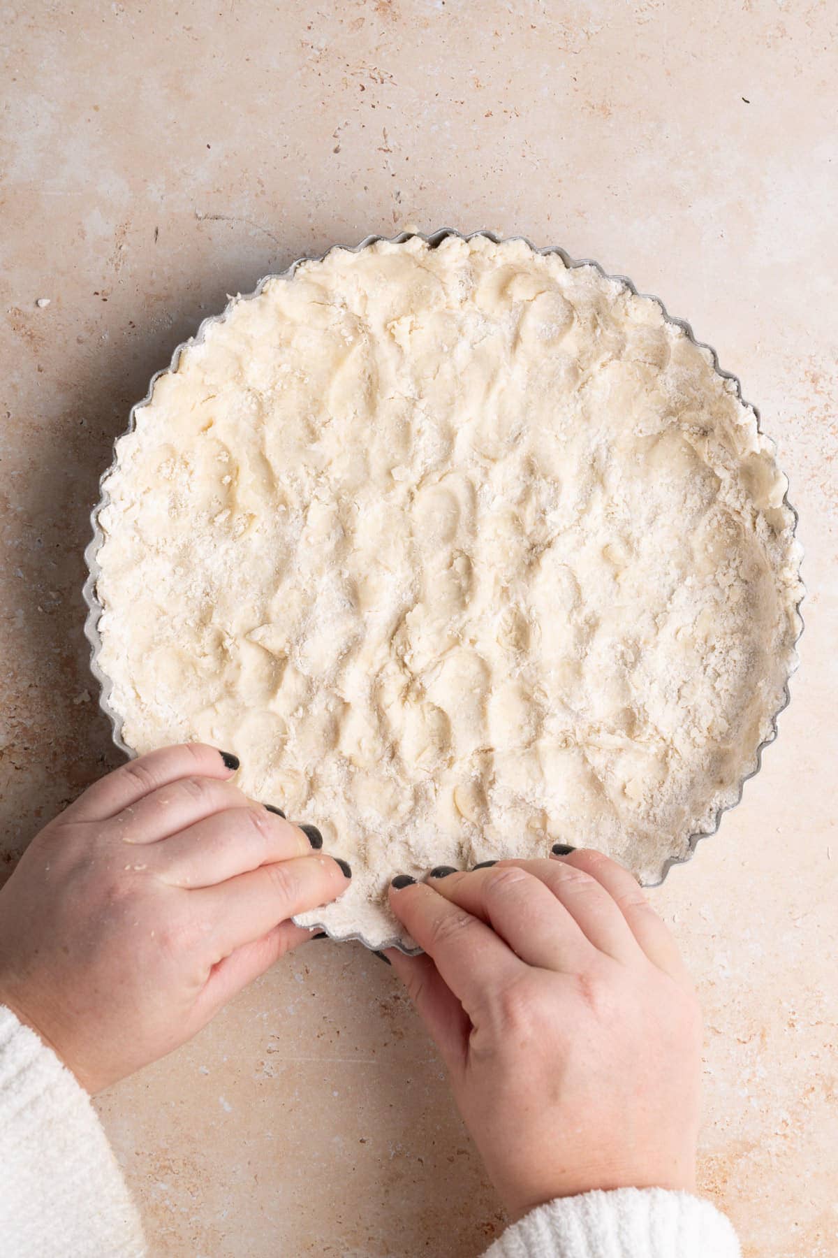 Using two hands to press crust into pie dish on the bottom and up the sides.