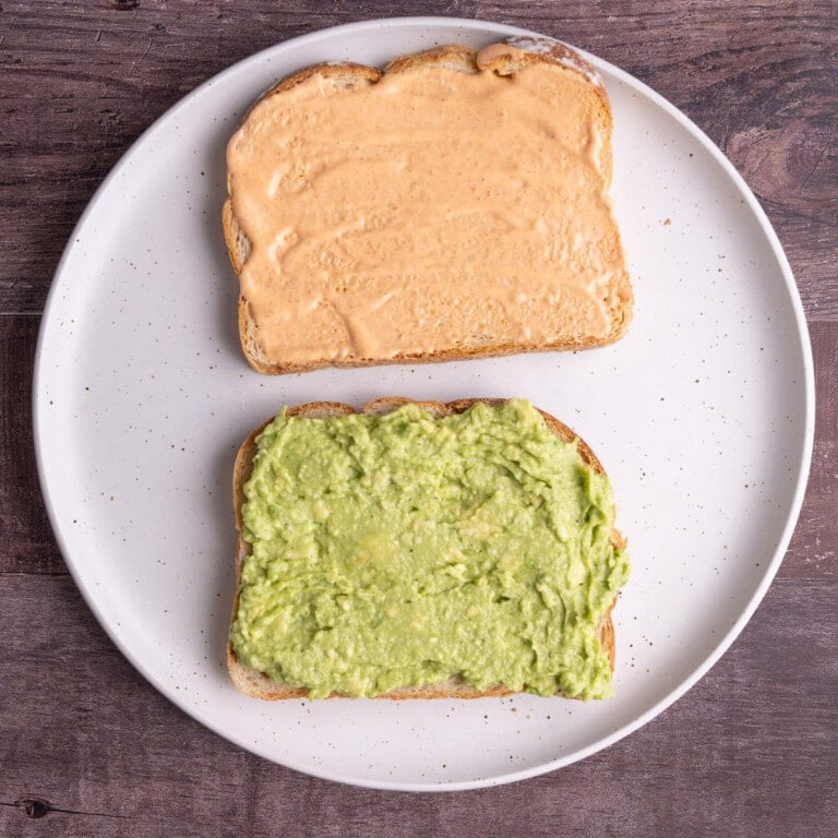 Two slices of bread, one with smashed avocado and one with spicy mayonnaise.