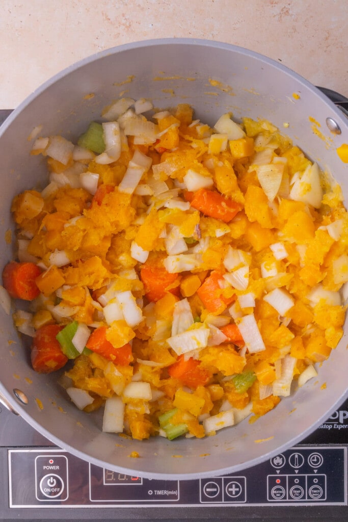 All vegetables for butternut squash based soup cooking down in a pot with butter, salt, and pepper.