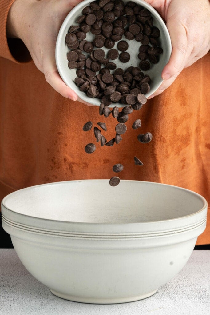 Adding chocolate chips to a mixing bowl with heavy cream to heat and make ganache.