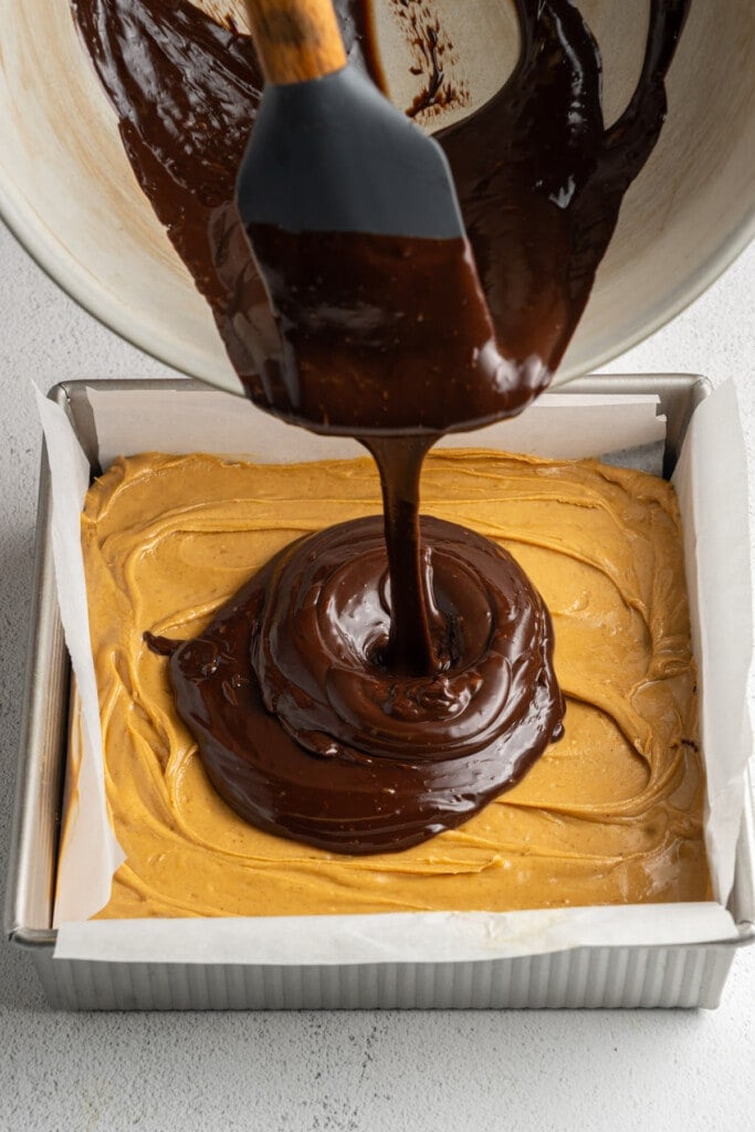 Pouring chocolate ganache over peanut butter layer on brownies.