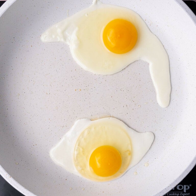 Two eggs frying in a pan until over easy.