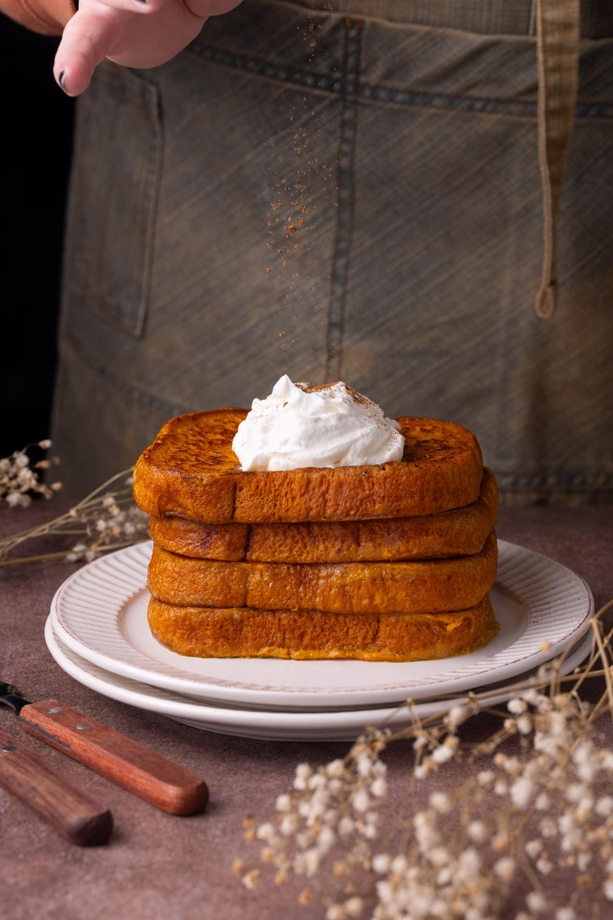 Sprinkling extra pumpkin pie spice on top of French toast with whipped cream.