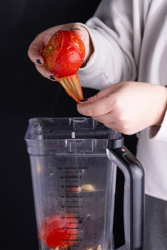 Peeling vine ripe tomatoes and adding them to a blender. 