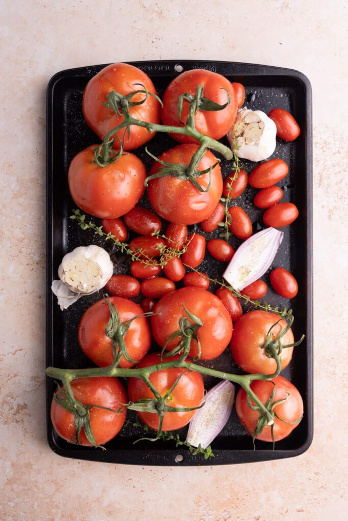 Tomatoes, shallot, garlic, and thyme lined up on a baking sheet to roast.