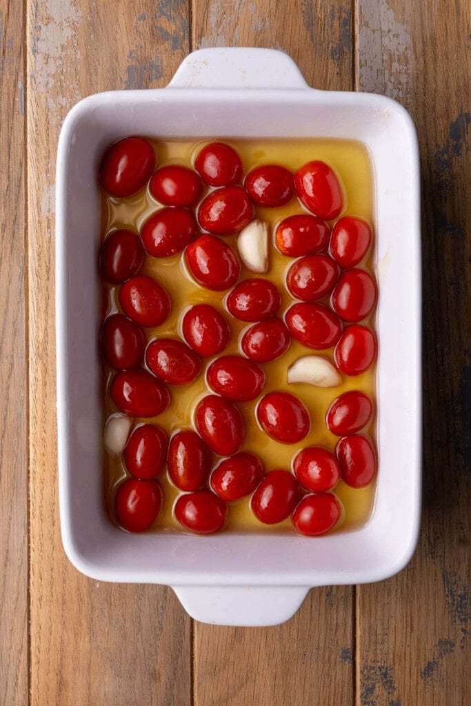 Grape tomatoes and garlic cloves submerged in olive oil with honey and salt.