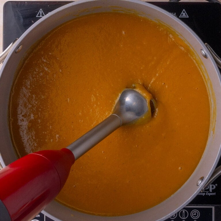 Blending Autumn Squash Soup with an immersion blender so that it is creamy and smooth.