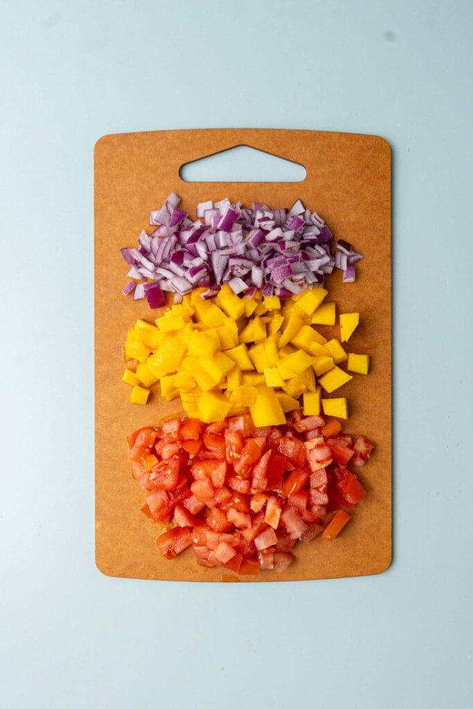 Diced red onion, mango, and tomato on a chopping board.