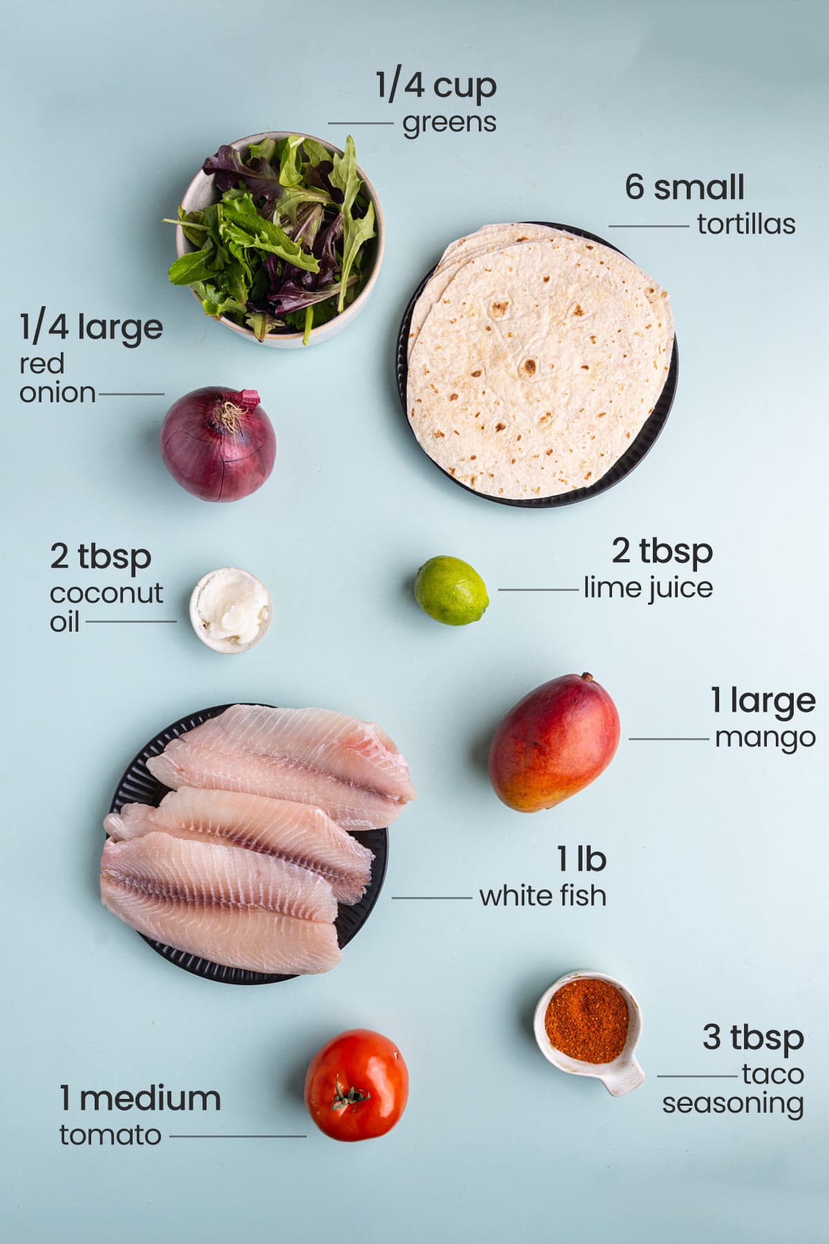 All ingredients needed for Fish Tacos with Mango Salsa including greens, tortillas, red onion lime, coconut oil, mango, fish, tomato, and taco seasoning. 