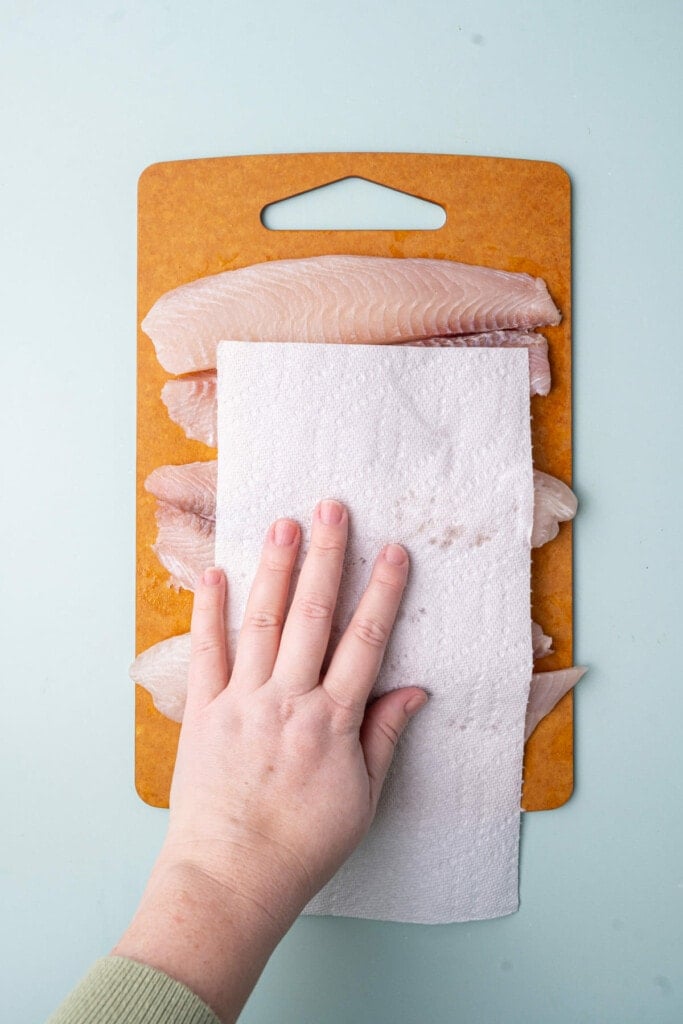 Using a paper towel to pat dry tilapia to reduce excess moisture. 