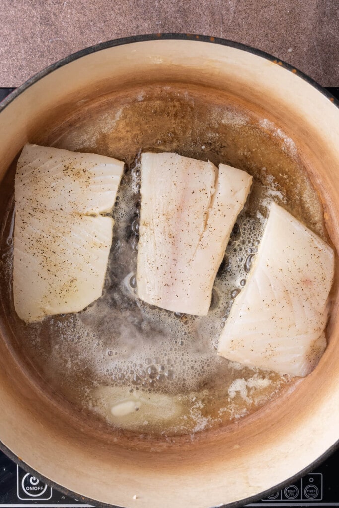 Halibut seasoned with salt and pepper searing in melted butter.