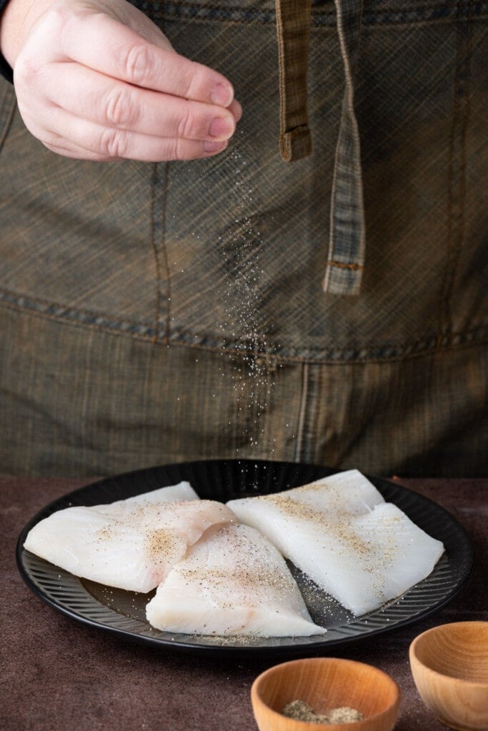 Adding salt and pepper to halibut that has been pat-dried with a paper towel.