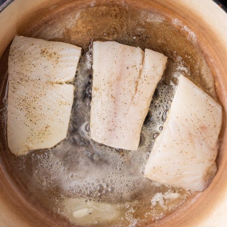 Seasoned halibut searing in melted butter.