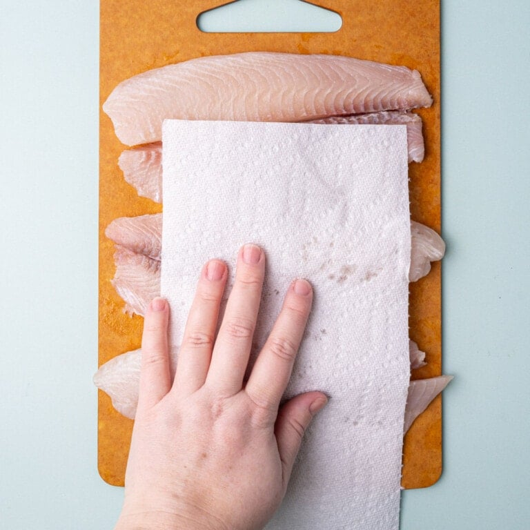 Using a paper towel to blot fish dry to remove excess moisture.