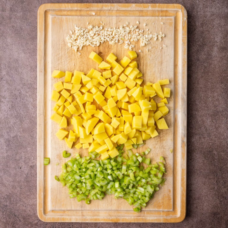 Minced garlic, peeled and diced potatoes, and diced celery on a cutting board.