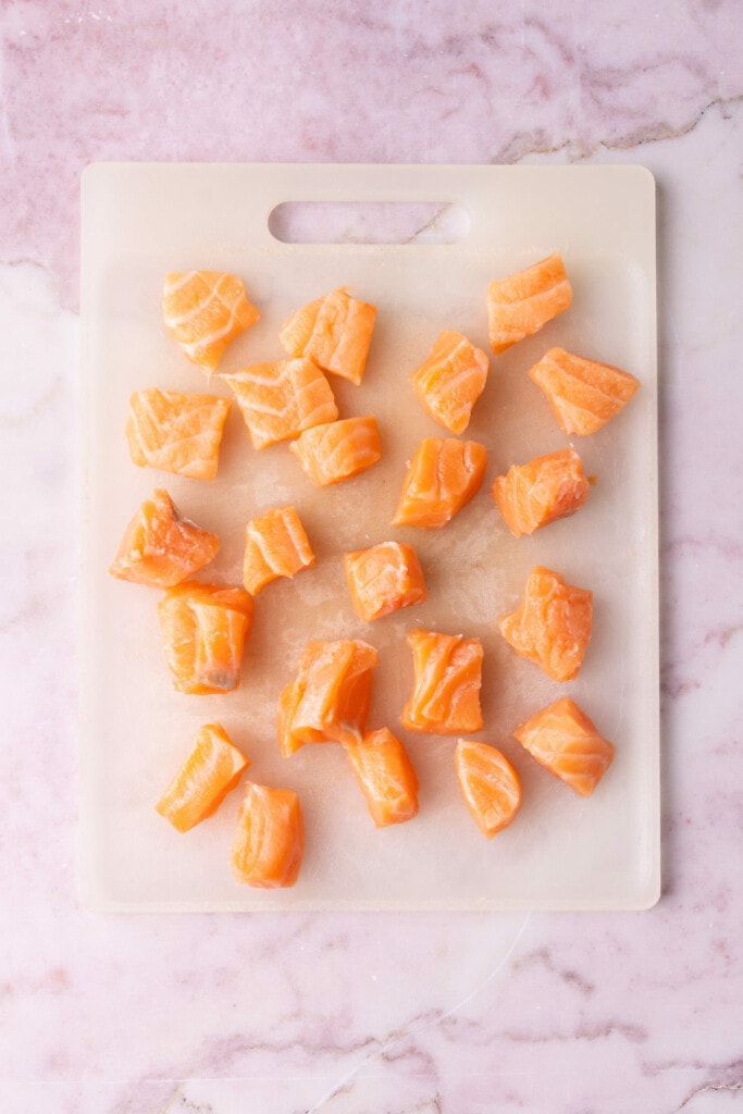Salmon on a chopping board cut into bite-sized cubes.