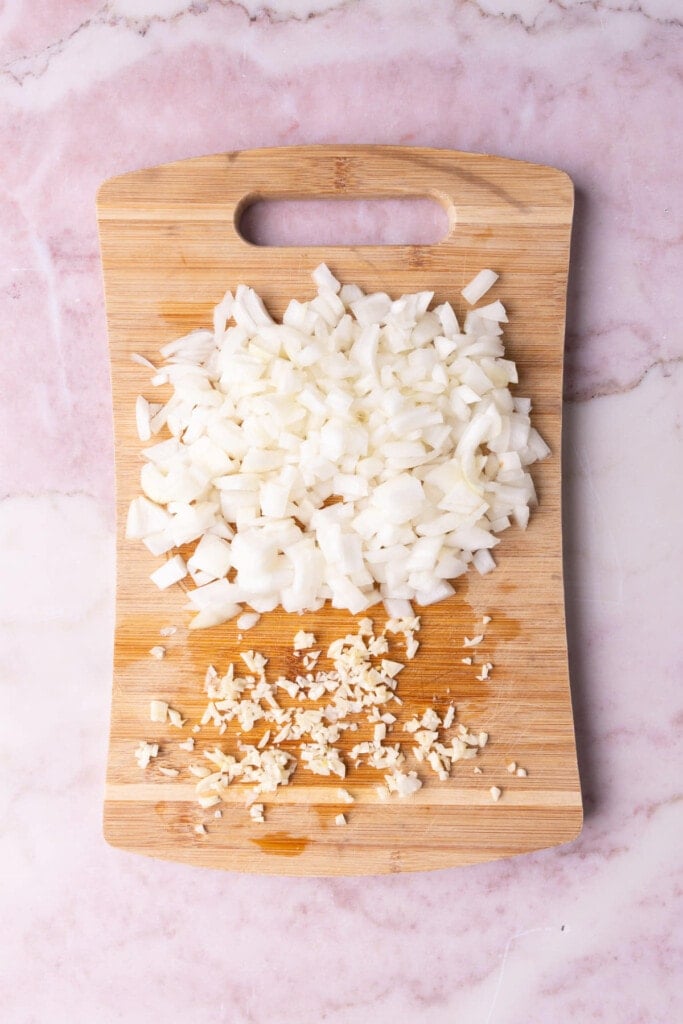 Chopping board with diced onion and minced garlic.