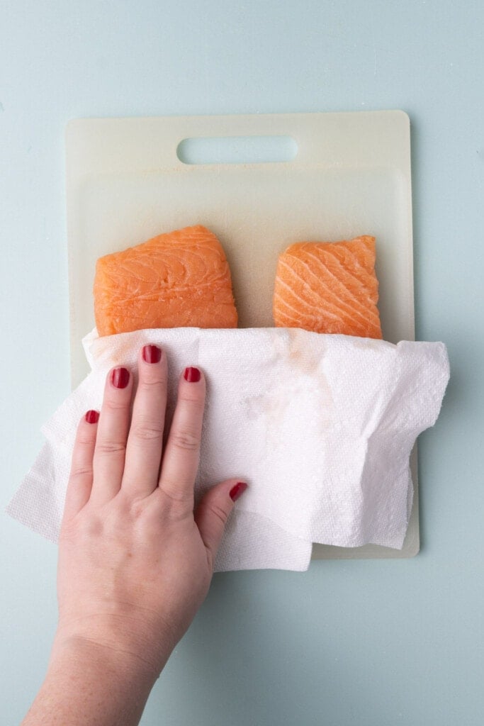 Blotting dry salmon with a paper towel to reduce excess moisture. 