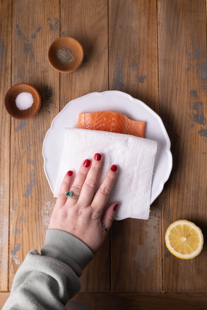 Using a paper towel to pat dry salmon and reduce excess moisture.