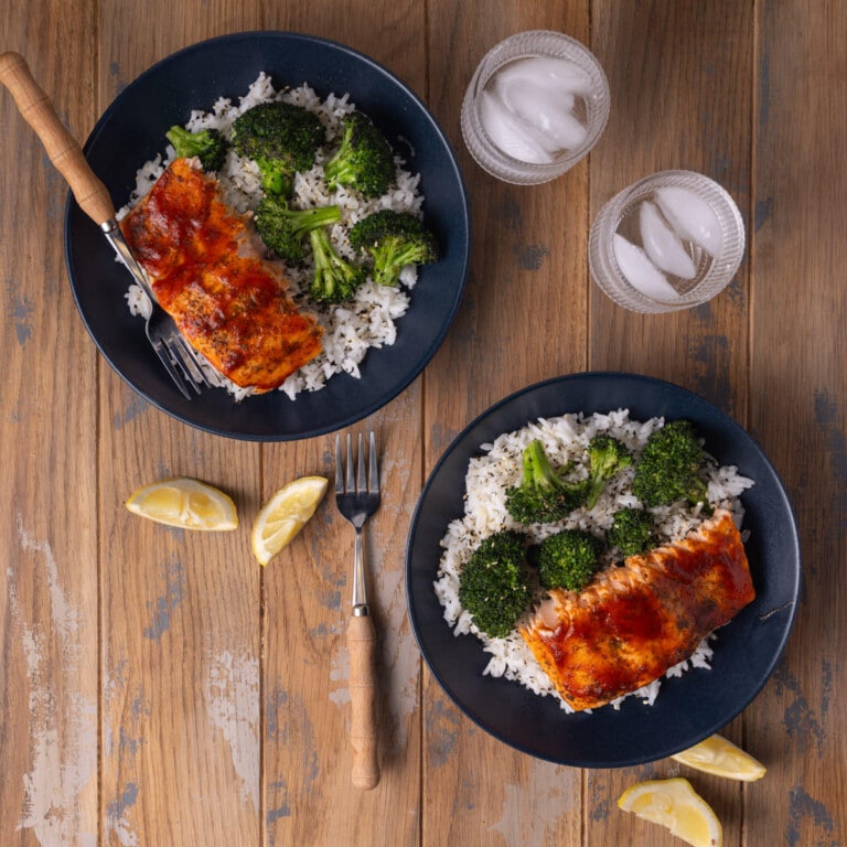 Two dinner plates with rice, broccoli, and honey sriracha salmon.