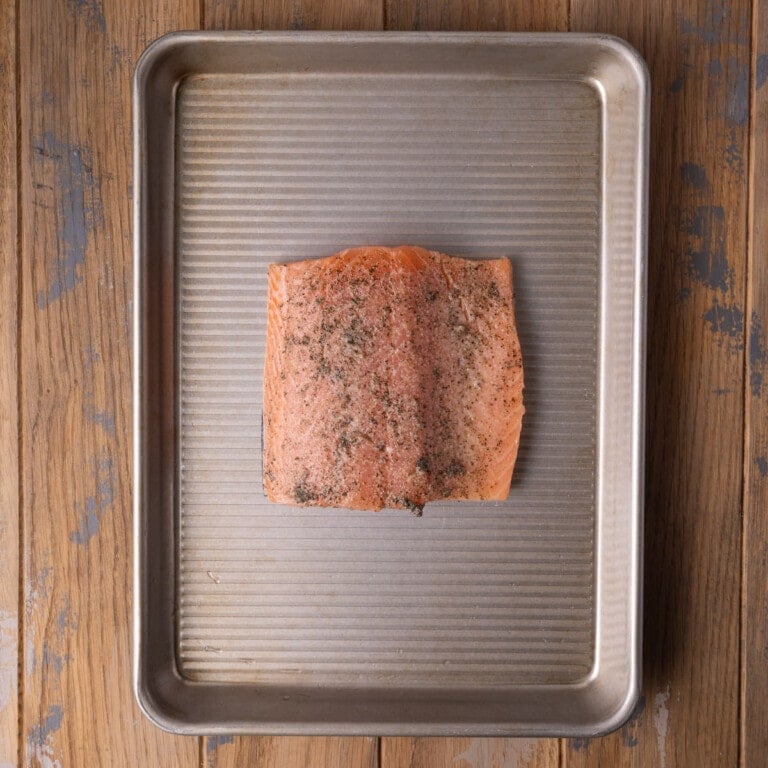Salmon with lemon juice, salt, and pepper on a baking sheet.