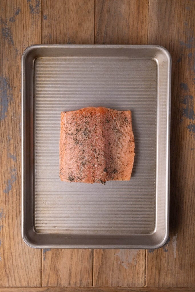 Salmon on a baking sheet with lemon juice, salt, and pepper ready to roast in the oven.