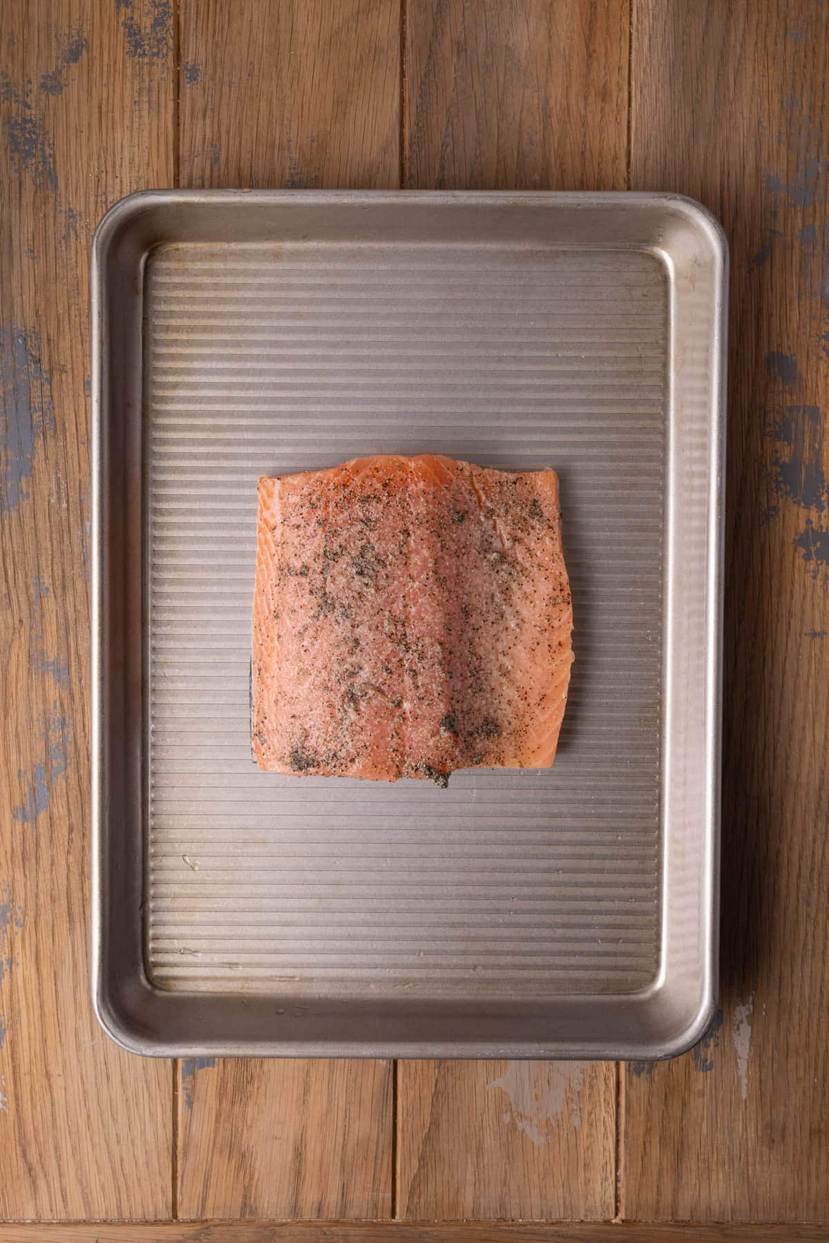 Salmon on a baking sheet with lemon juice, salt, and pepper ready to roast in the oven. 